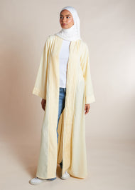 This open pleat abaya in buttercream boasts exquisite neat pleating that cascades down the placket and cuffs, offering a loose yet structured fit for all body types. Perfect as a quick cover-up for everyday outfits, or paired with one of our full slips for a more elegant ensemble.