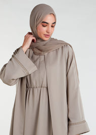 This open abaya in beige is the perfect addition to any wardrobe. Its loose fit and neutral colour make it versatile and suitable for a variety of outfits. The delicate lace trim adds a feminine touch to complete the look.