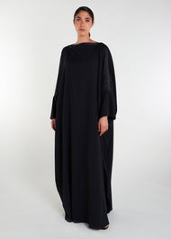 This loose fit classic black kaftan features a luxurious satin strip across the neck line and sleeves, adding an elegant touch to its modest cut silhouette. Ideal for various occasions.